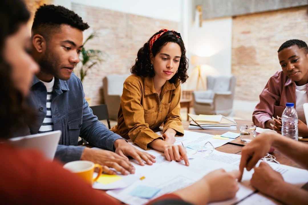 A group of people gathered around a table covered with papers, collaborating and discussing ideas in a team setting.